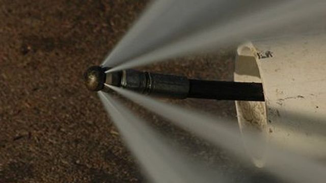 Water jetting from a nozzle into a pipe, on a brown surface.