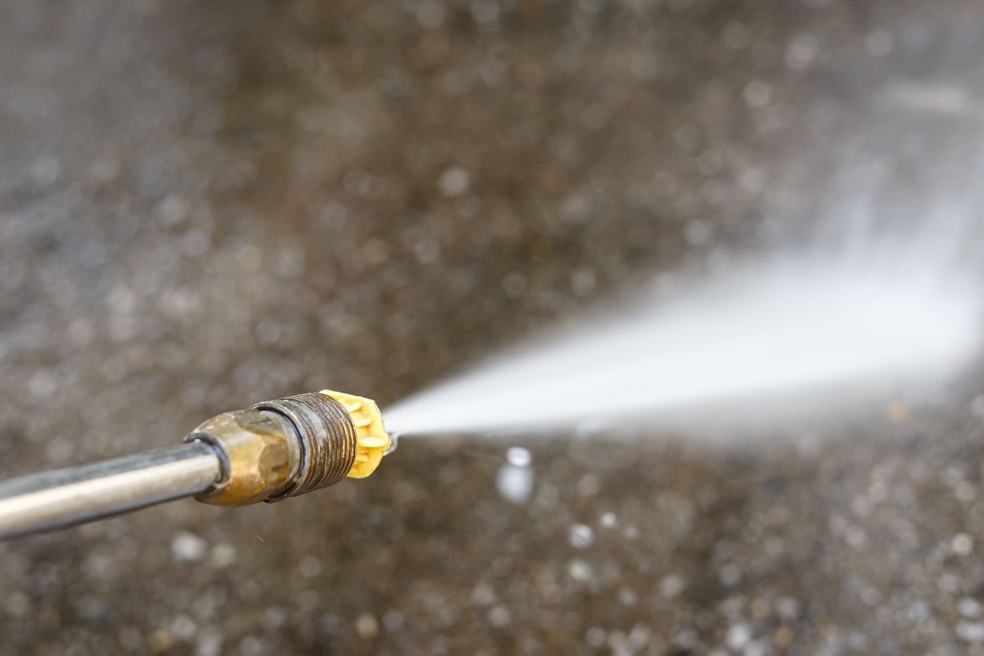 A pressure washer nozzle sprays water onto a concrete surface.