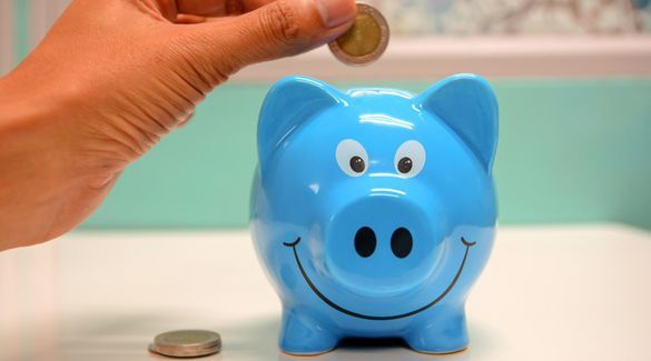 A person is putting a coin into a blue piggy bank.