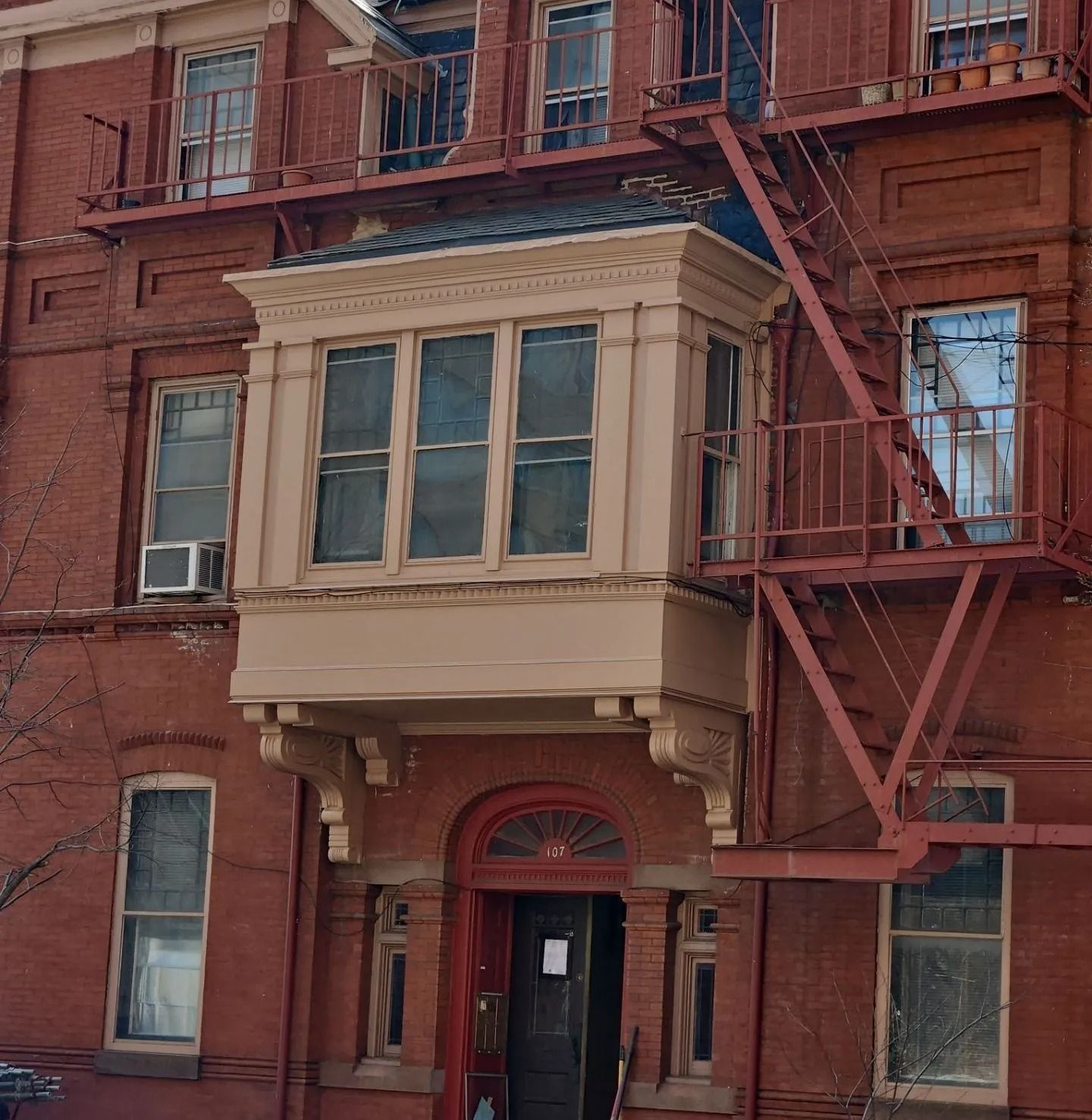 Red brick building with a bay window, fire escape, and arched doorway.