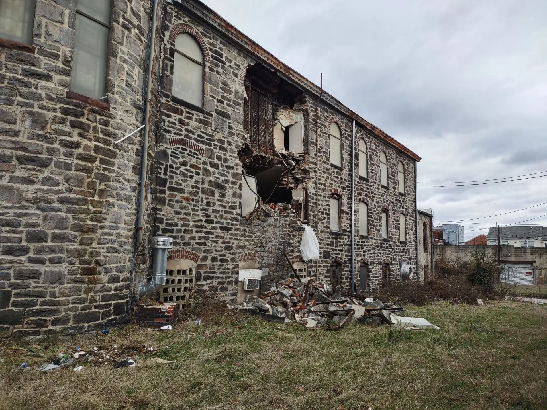Damaged stone building with a collapsed section of the wall; debris on the ground; overcast sky.