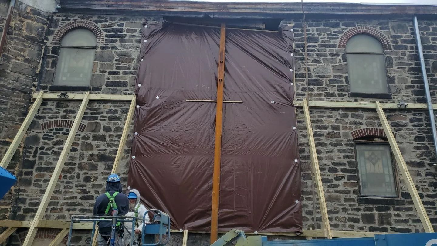 Building facade with brown tarp covering an opening, supported by wooden beams. Workers on lift.