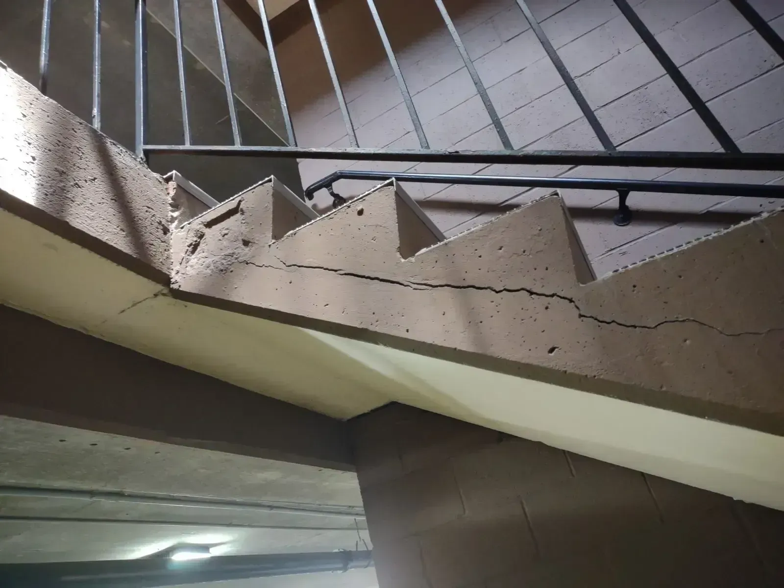 Cracked concrete staircase with a metal handrail. Brown walls and a gray staircase.