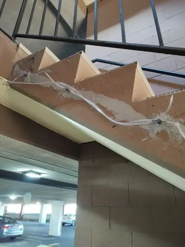 Stairwell leading to a parking garage. Brown and beige steps, metal railing, cobwebs.