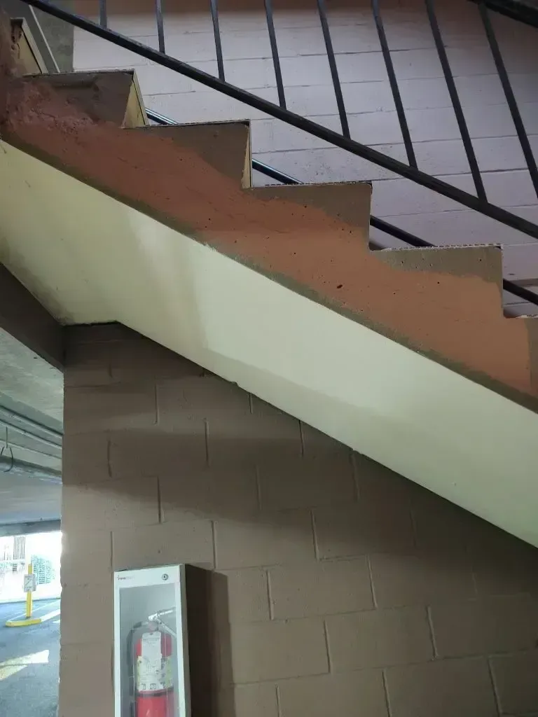 Staircase with brown brick wall, fire extinguisher, and metal railing. Stairs are tan with a white underbelly.