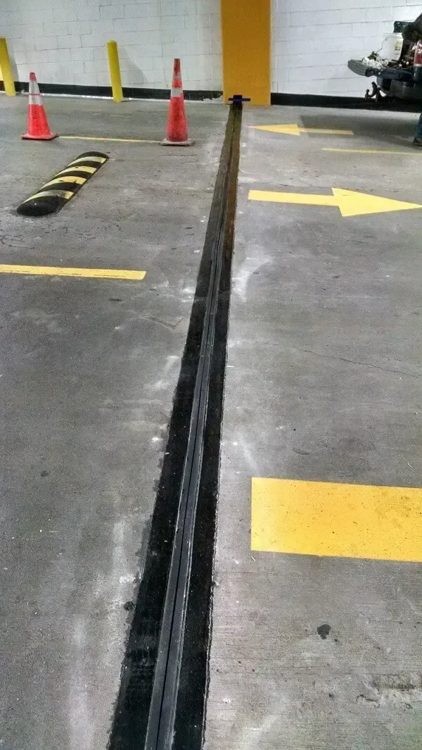 Concrete parking garage floor with a long black expansion joint, traffic cones, and yellow painted arrows.