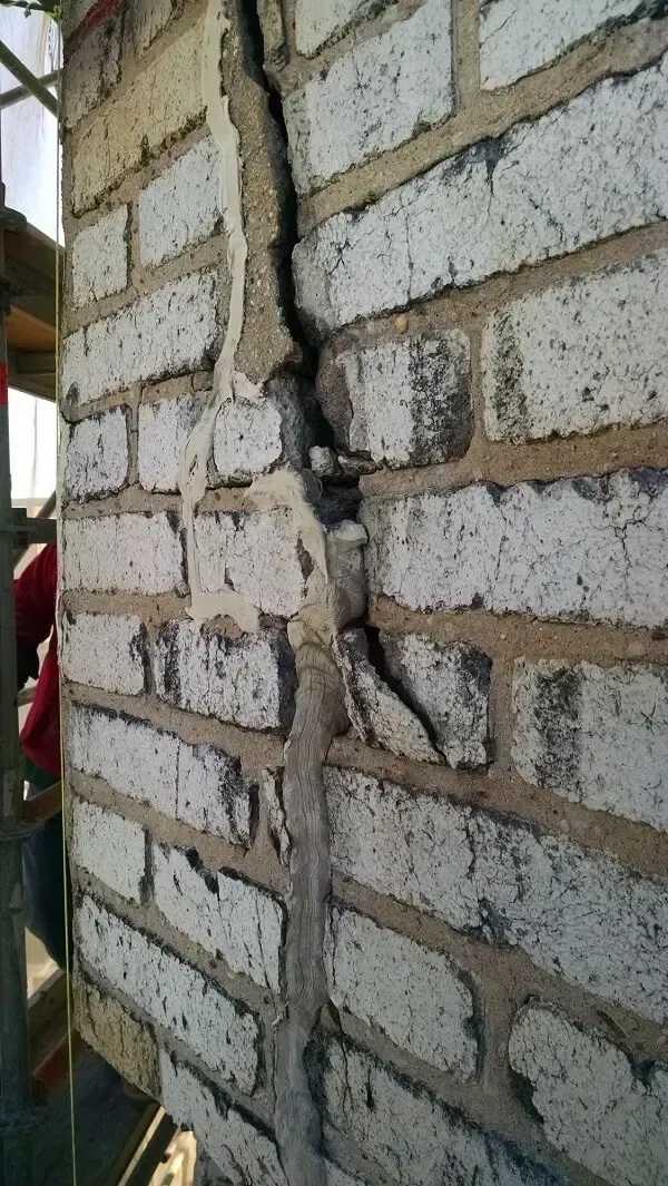 Close-up of a brick wall with a large vertical crack filled with repair material. White bricks, tan mortar.