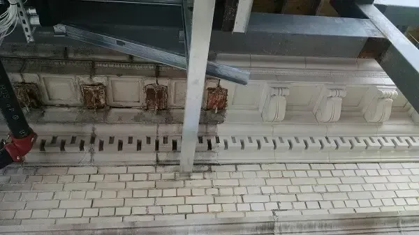 Brick wall with ornate white molding, metal beams overhead, and pipes.