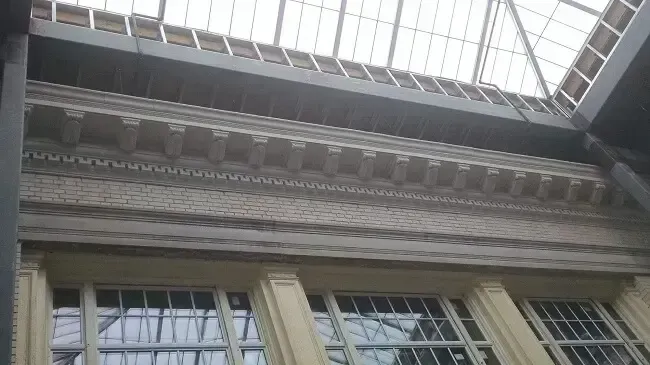 Interior view of ornate building facade with windows, moldings, and glass ceiling.