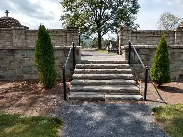 Stone steps leading through a stone wall with handrails and evergreen trees.