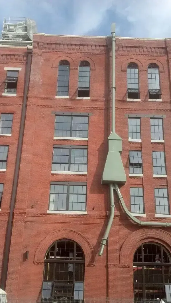 Red brick building with arched windows, multiple floors, and a green ventilation system.
