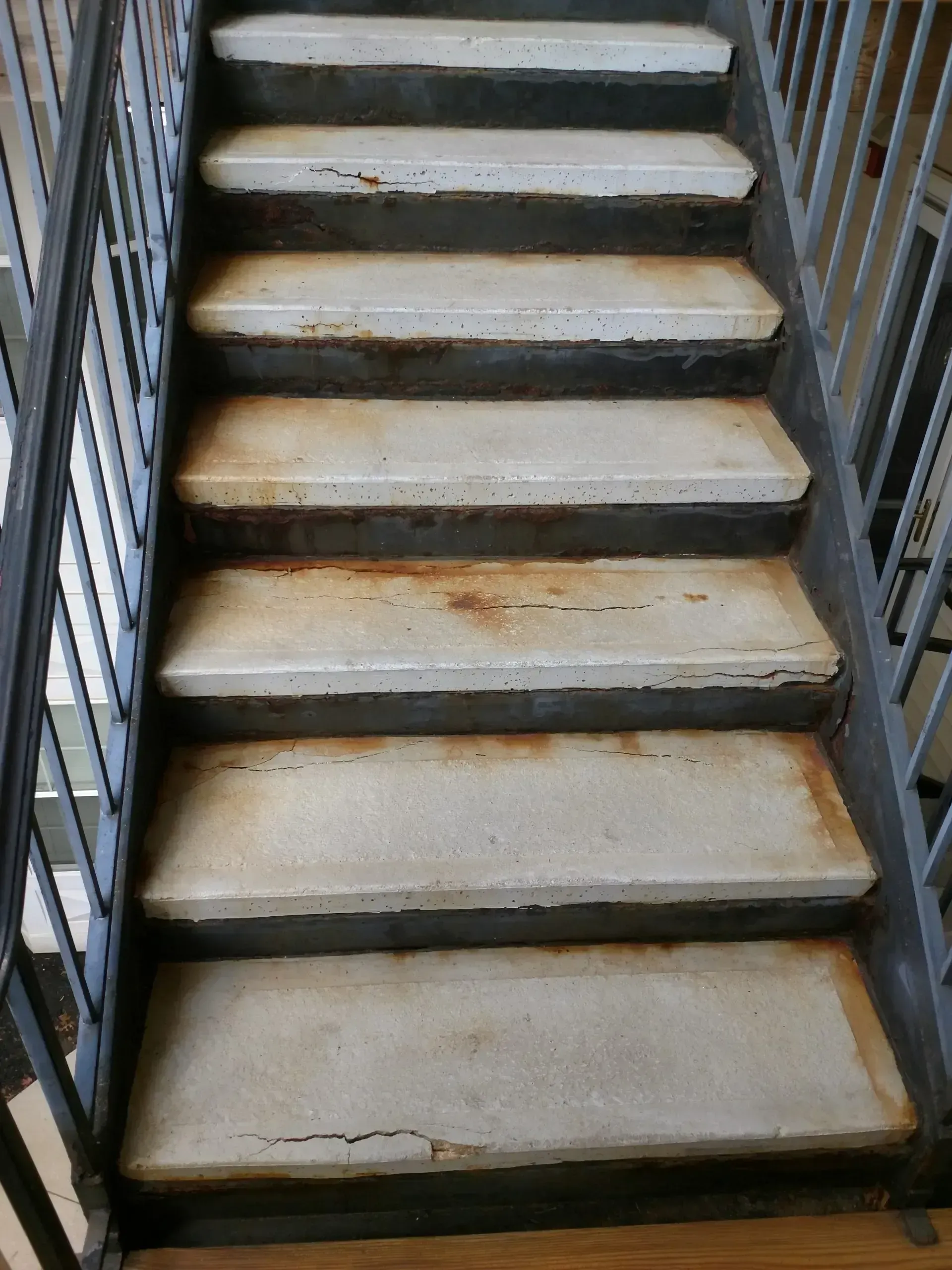 Concrete staircase with metal handrail. Worn, stained steps. Interior setting.