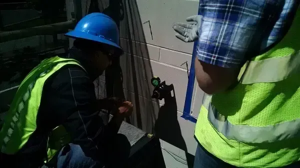 Two workers in safety vests and hard hats examining a wall, one using a laser level.