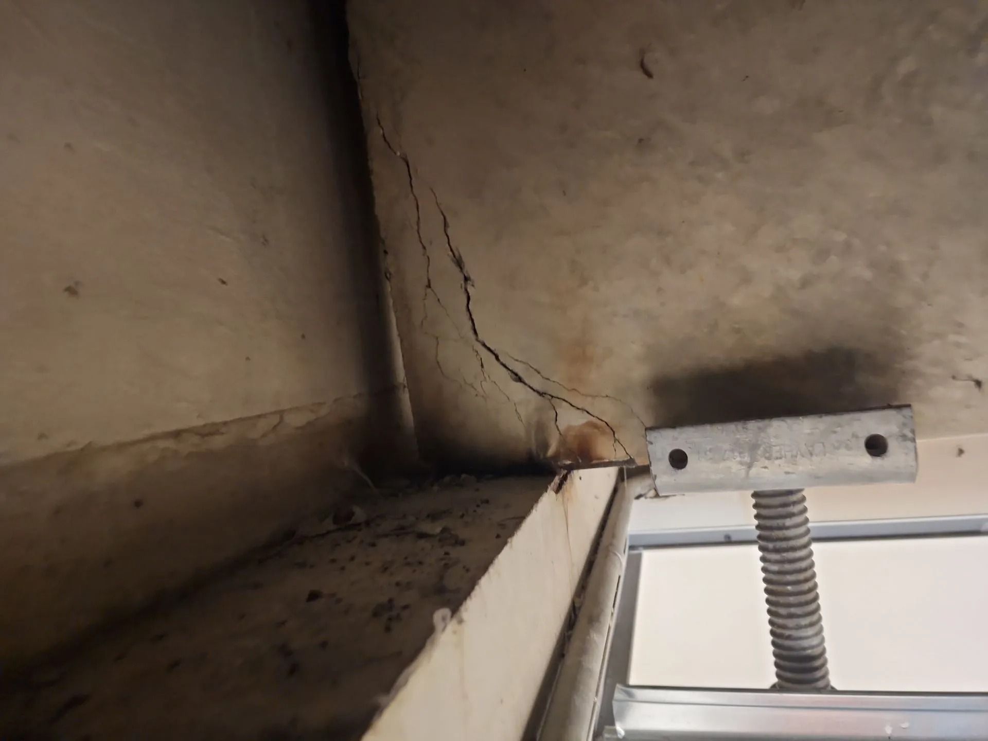 Crack in the corner of a ceiling, possibly concrete, with a support jack visible.