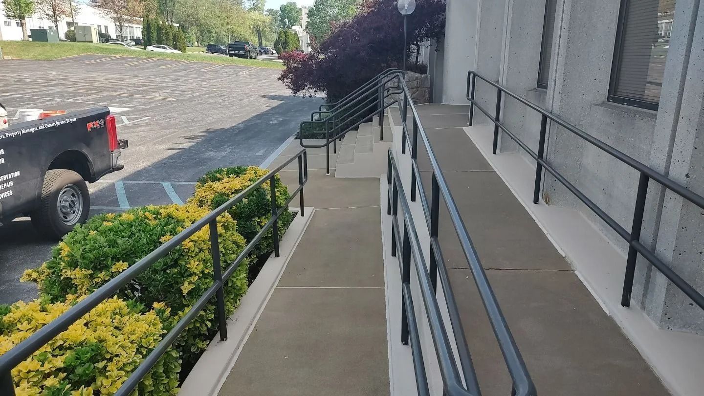 Ramp with black handrails leading up to a building entrance; a pickup truck and greenery are visible.