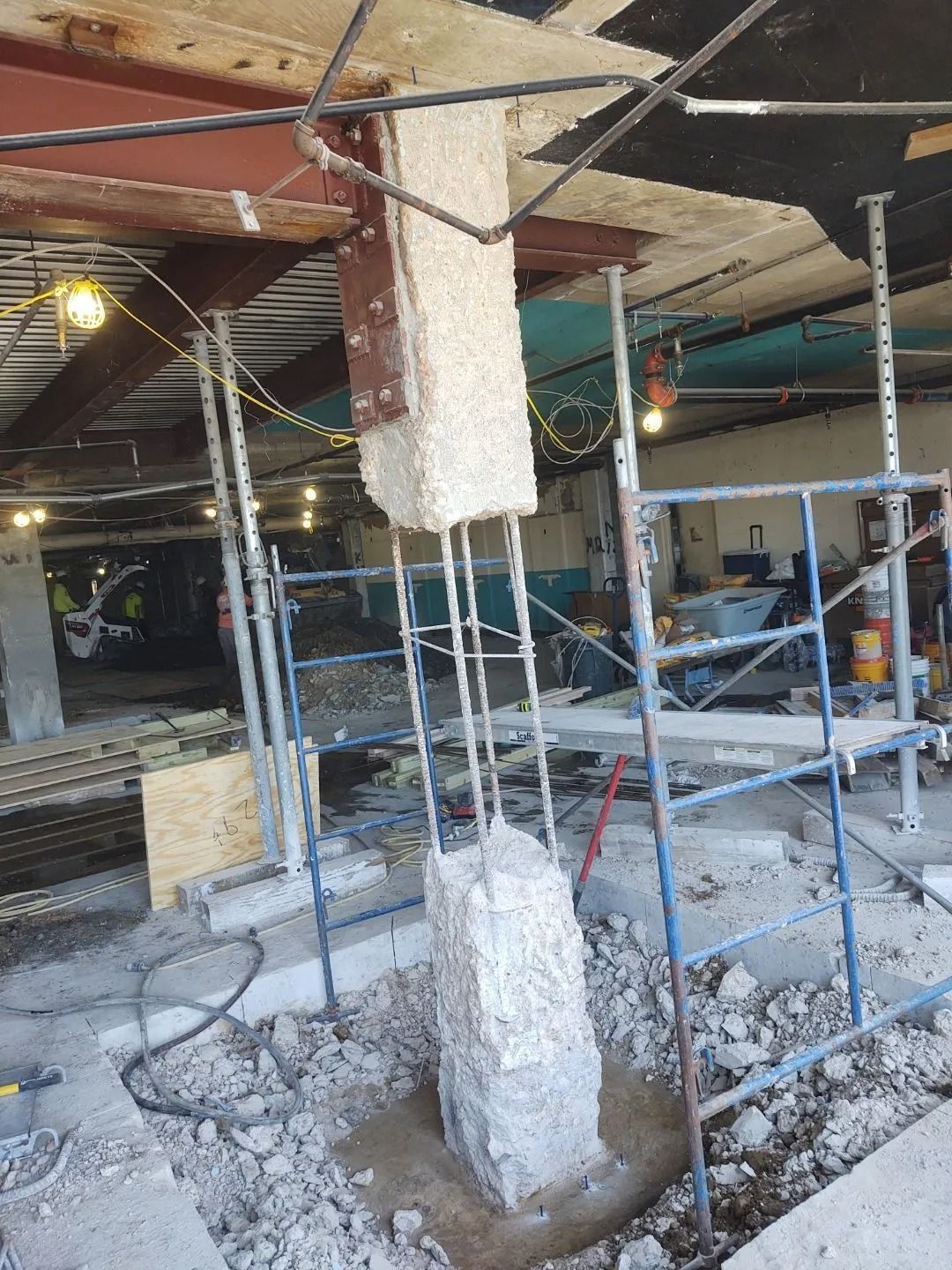 Construction site with a concrete column being worked on, scaffolding and steel beams are present.