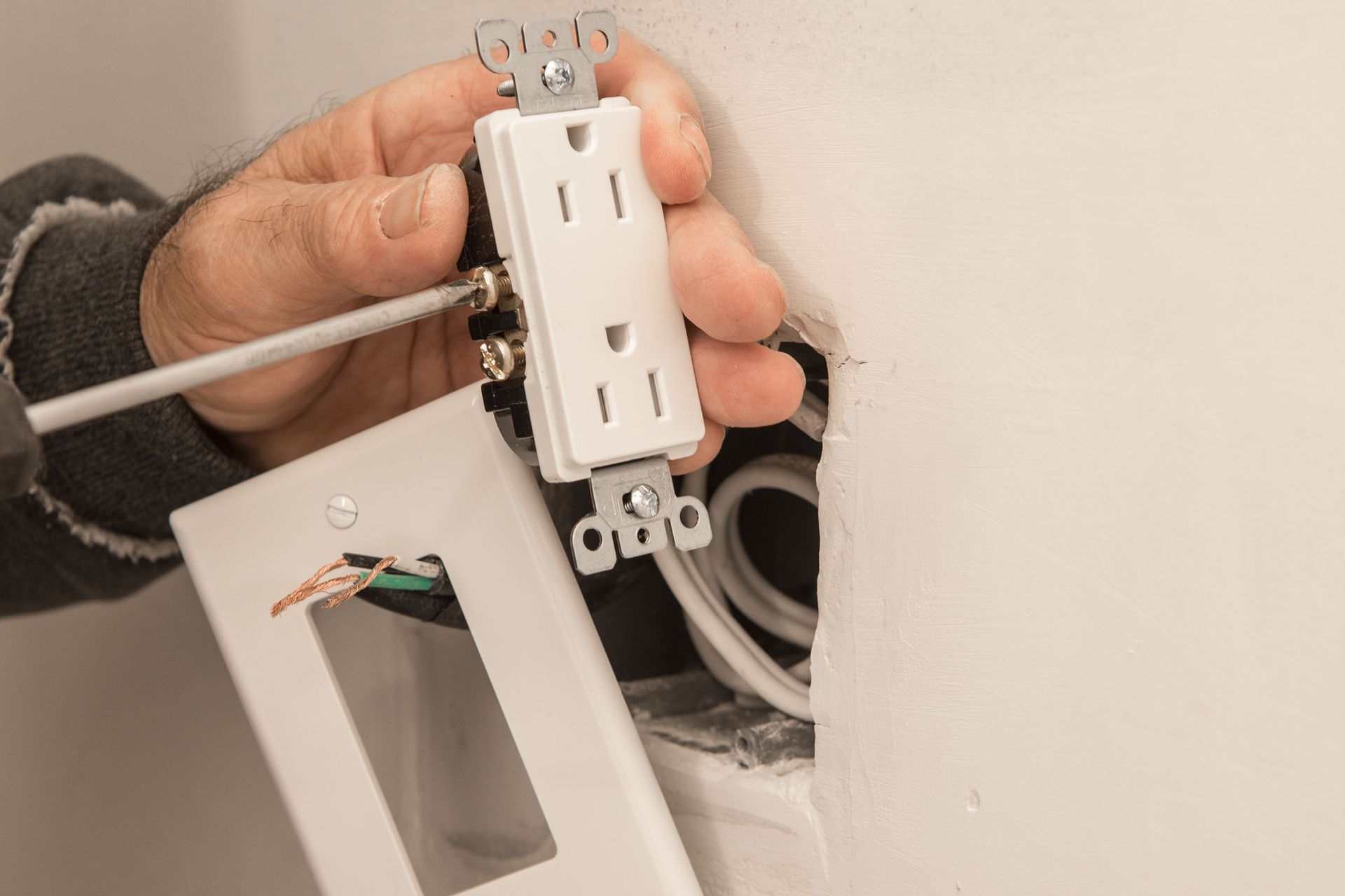 Person installing electrical outlet in a wall, using a screwdriver.
