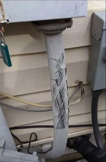 White insulated pipe with damaged covering, attached to an outdoor electrical box.