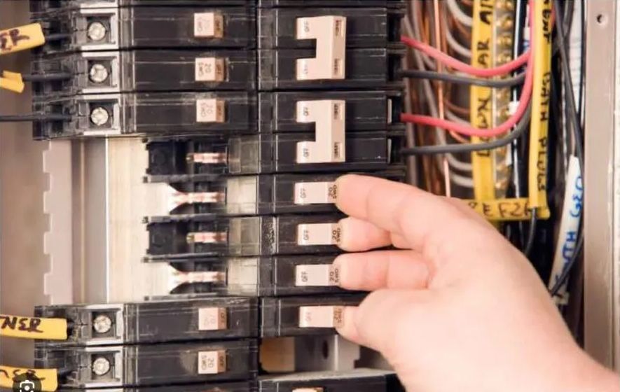 Hand touching a circuit breaker in an electrical panel, likely turning it off.