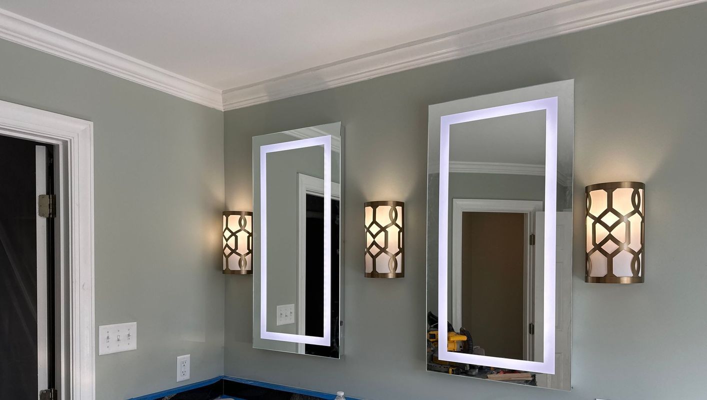 Bathroom with backlit mirrors and decorative wall sconces on gray walls.