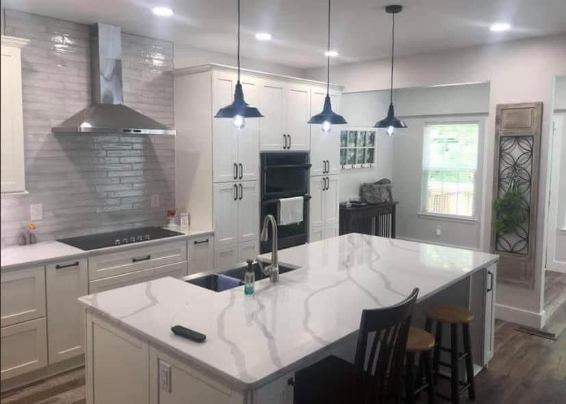 Modern white kitchen with island, pendant lights, and stainless steel range hood.