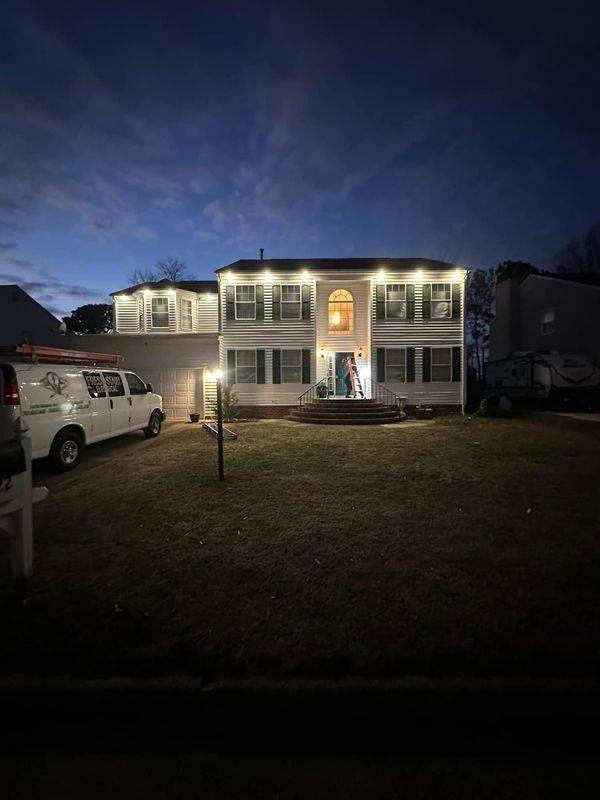 Two-story white house with lights on, van parked in front, grass yard, dusk sky.