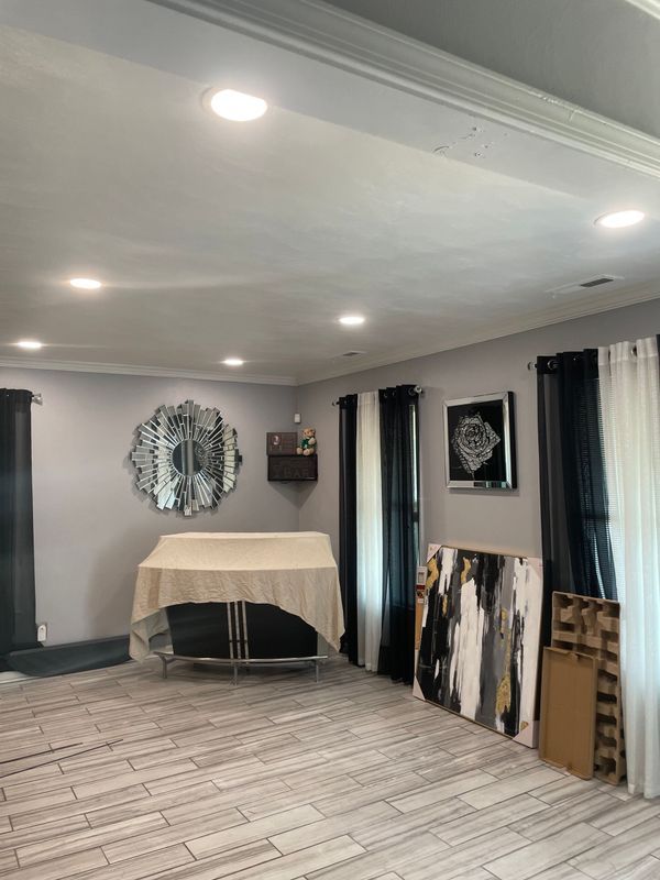 Living room with light gray walls, wood-look floor, art, black and white curtains, and a table covered with a tan cloth.