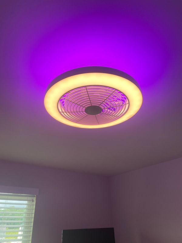 Ceiling fan with a circular light, emitting yellow light and a purple glow above.