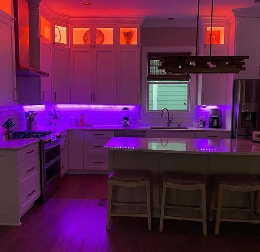 Kitchen with white cabinets, purple and orange LED lighting, and island with stools.