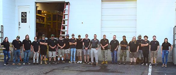 A group of people posing in front of a white building with an open door.