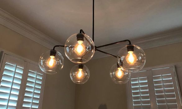 Five-bulb chandelier with clear globe shades, hanging from a black rod, in a room with white shutters.