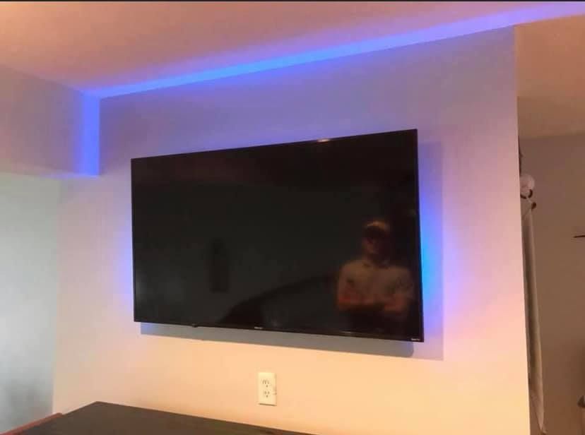 Wall-mounted TV with blue LED strip lighting. A person is reflected in the screen.