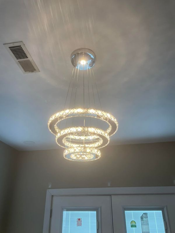 Three-tiered, glowing crystal chandelier hanging from a white ceiling, above a white door with two panes.