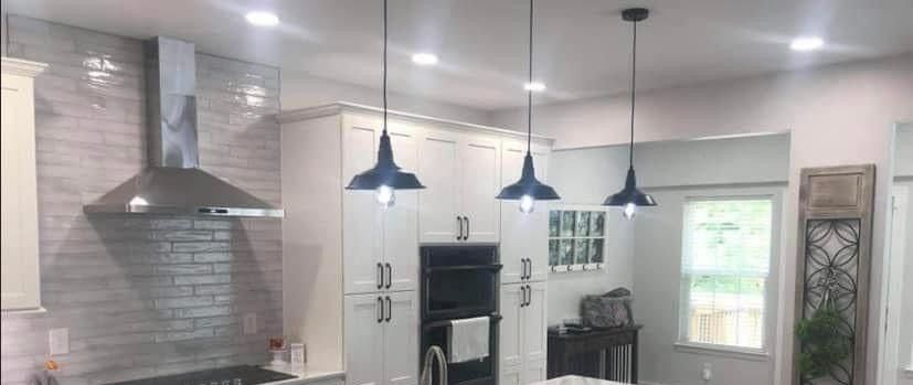 A well-lit modern kitchen with white cabinets, dark pendant lights, and stainless steel range hood.