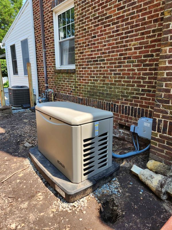 Tan generator installed on a black pad near a brick building.