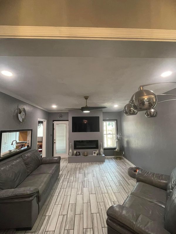 Living room with gray walls, white tile floor, two gray leather sofas, and a fireplace with a mounted TV.