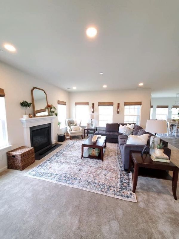 Spacious living room with a fireplace, dark sofa, patterned rug, and neutral walls.