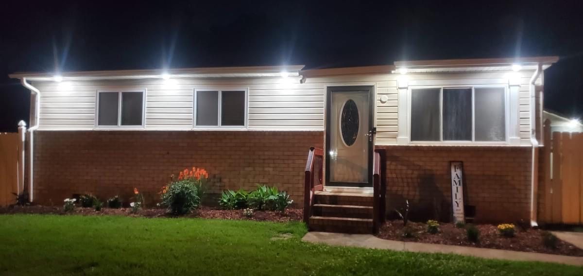 A house at night with lights on, front yard and a flower bed. Brick and siding exterior.