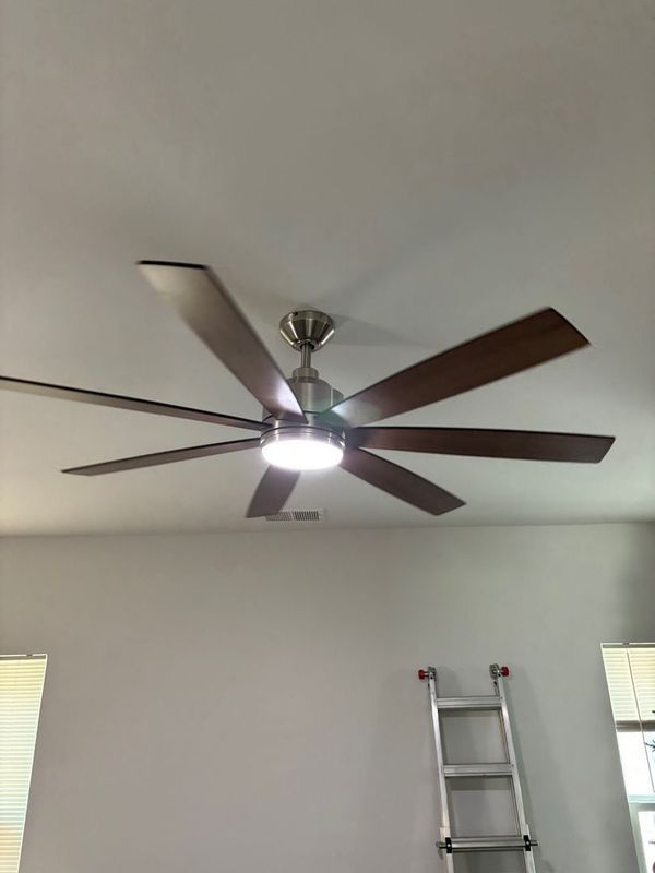Ceiling fan with dark wooden blades and a central light fixture. A ladder is positioned near a window.