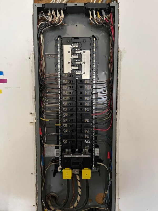 Electrical panel with circuit breakers and wires. Black and gray components. Mounted in a wall.