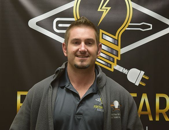 Man wearing a gray fleece jacket stands in front of a logo with a light bulb, lightning bolt, and tools.