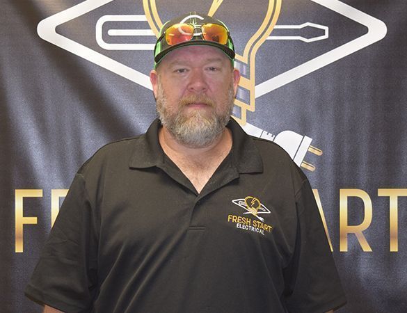 Man in a black polo shirt, wearing sunglasses on cap, in front of a logo with text.