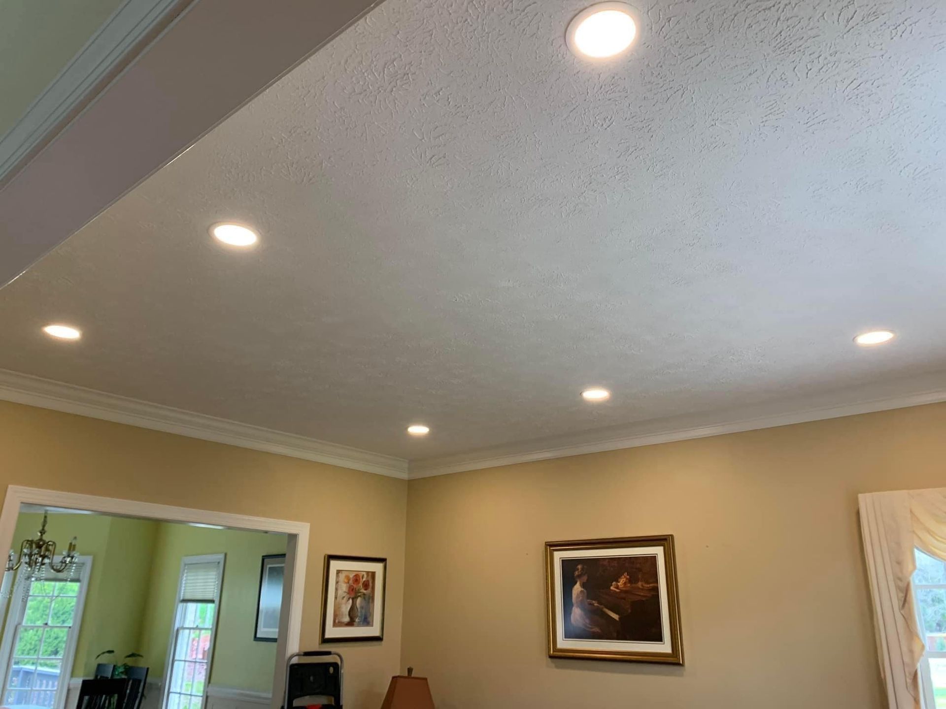 A room with recessed ceiling lights, crown molding, beige walls, and framed art.