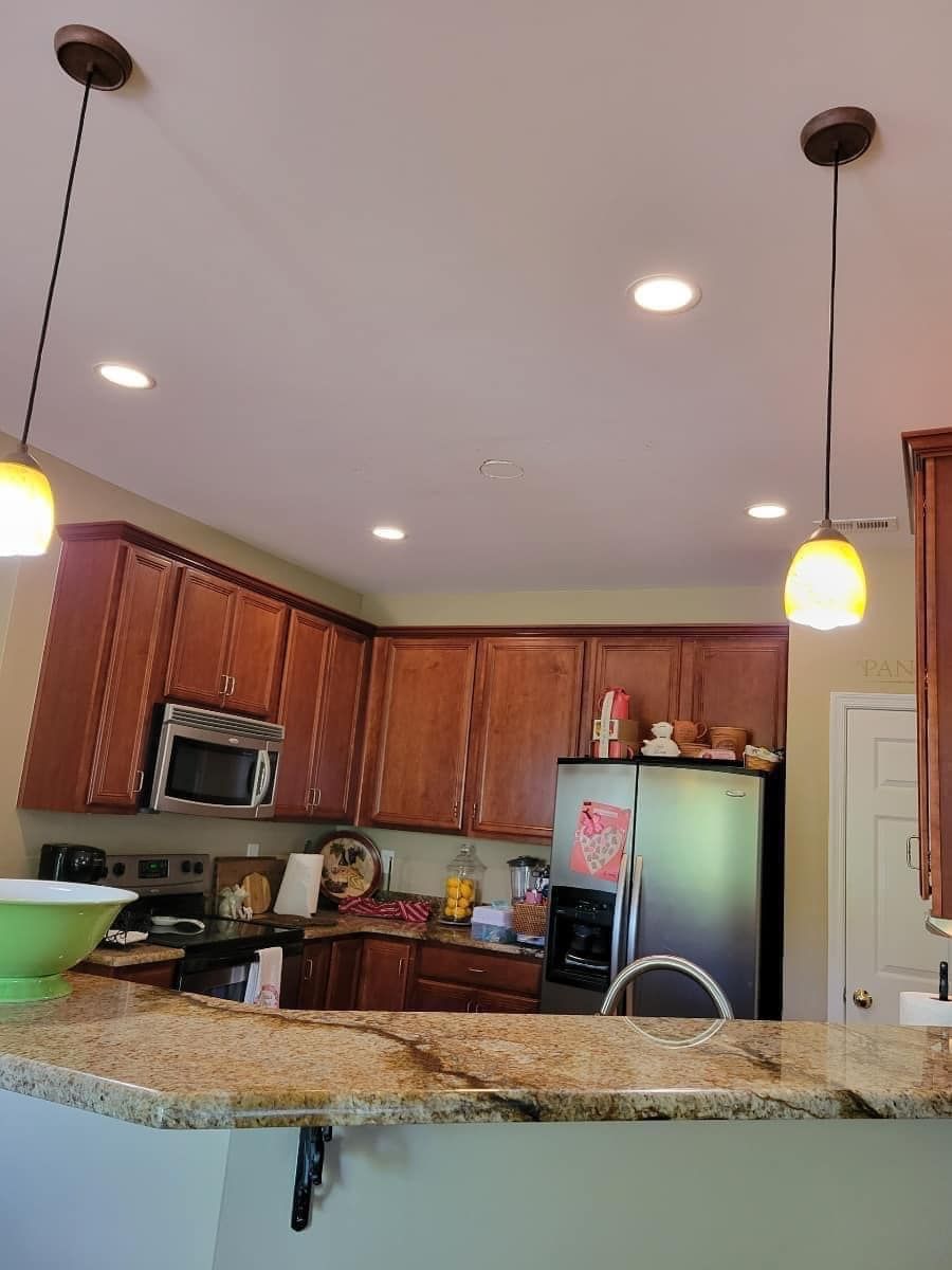 Kitchen with brown cabinets, stainless steel refrigerator, and two pendant lights over a countertop.