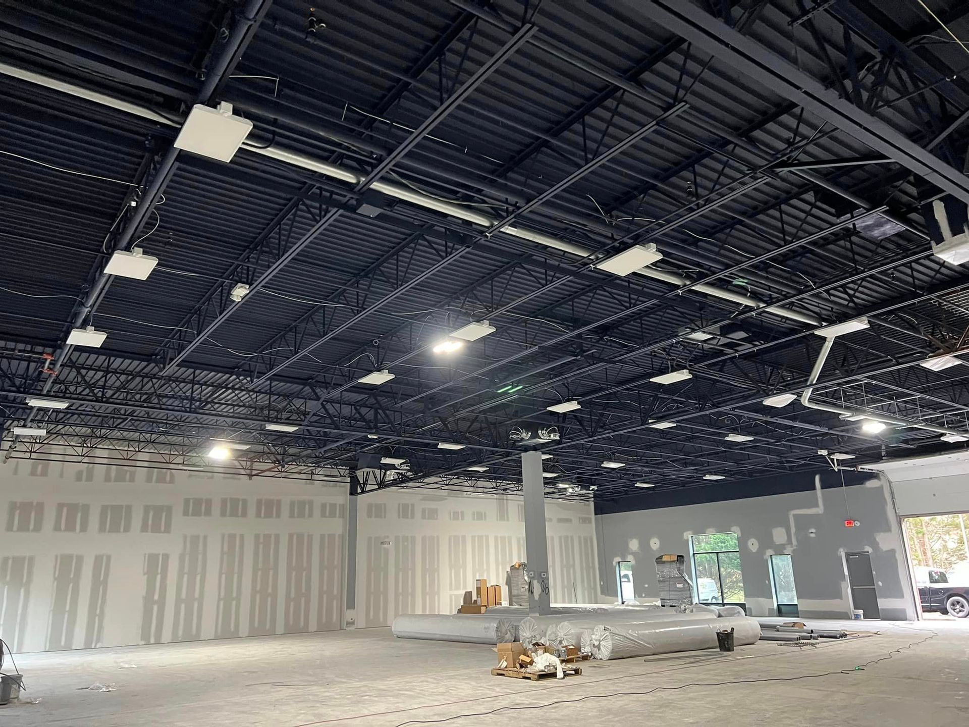 Construction site interior with exposed black ceiling, unfinished walls, and scattered materials.