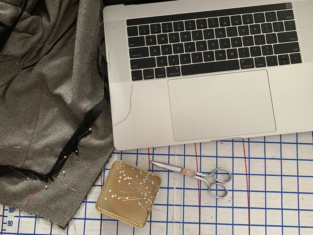 Laptop, fabric, sewing pins, and scissors on a grid cutting mat.