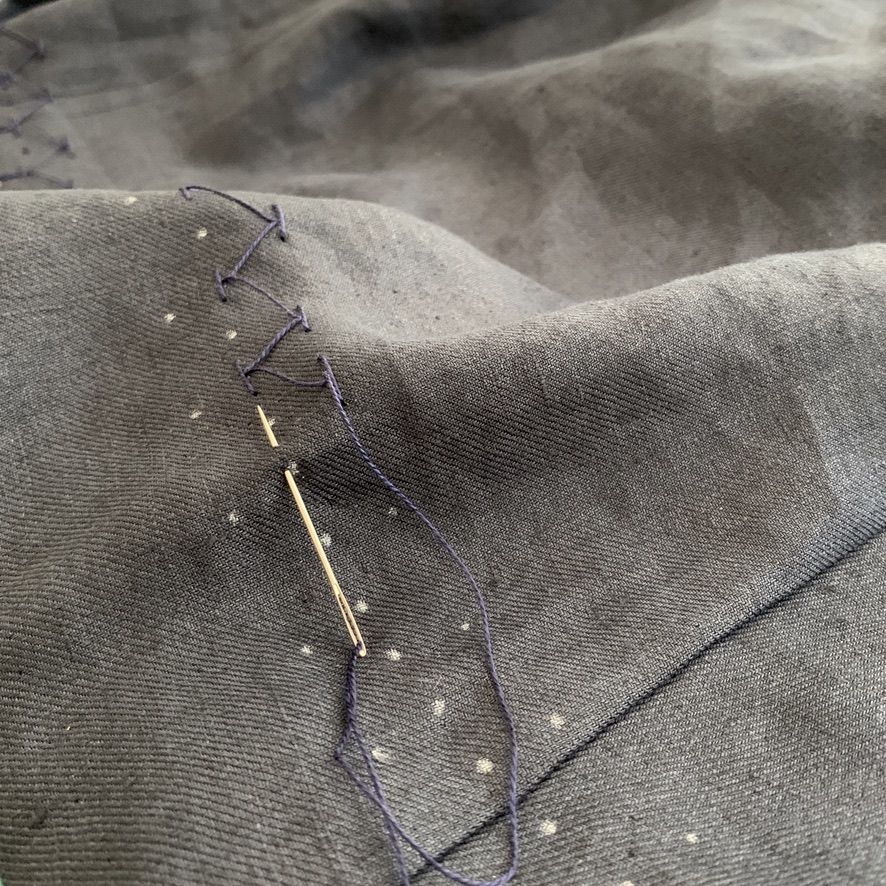 Needle and thread stitching dark denim fabric, repairing a seam.