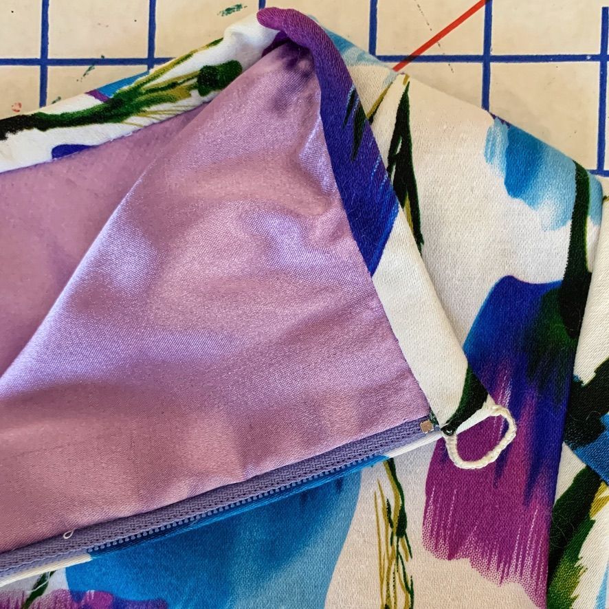 Close-up of a skirt's inside, showing the lining and zipper with a white floral pattern and purple fabric.