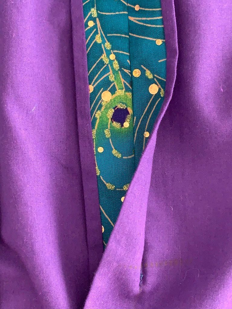 Purple fabric with teal and gold peacock feather trim, a buttonhole visible.