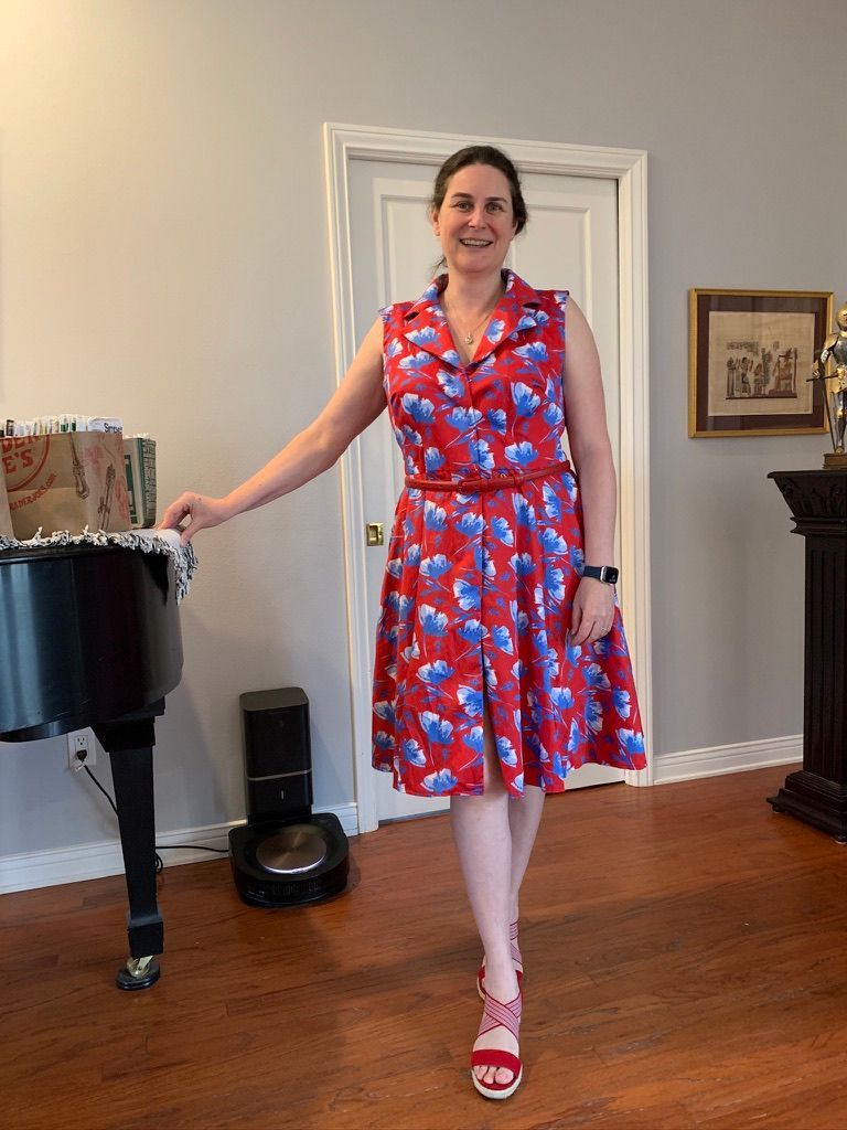 Woman in red floral dress, smiling, next to piano, wooden floor.